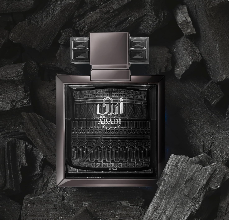 Zimaya Abadi dark square perfume bottle with patterned glass, silver lettering and broad geometric cap, nestled among black charcoal-like pieces.