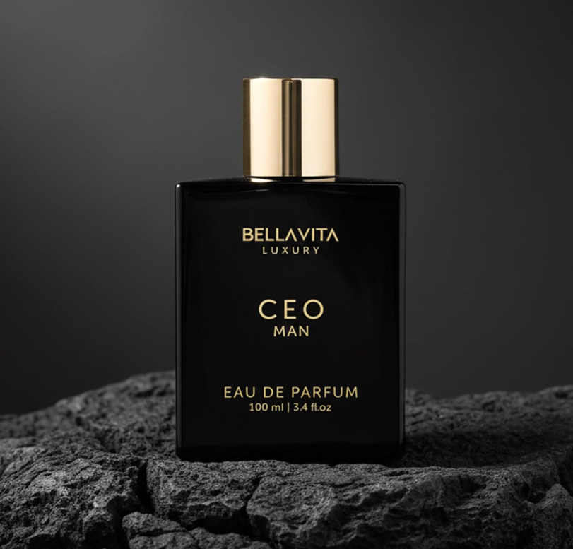 Bellavita CEO Man black perfume bottle with a gold cap and lettering standing on rough dark rock against a charcoal-gray background.