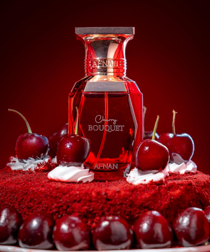 Afnan Cherry Bouquet red bottle on a red cake-like surface among cherries and white cream, with more cherries in the foreground and a dark red background.