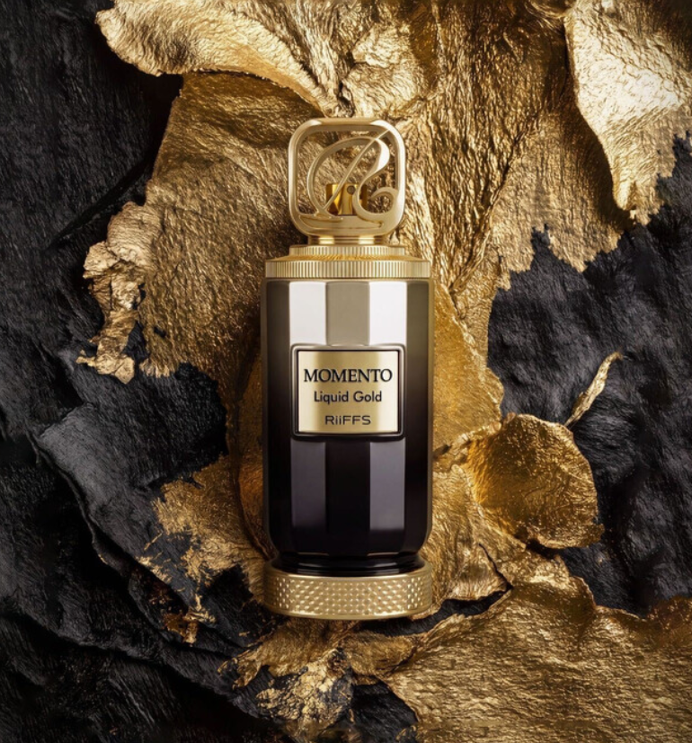 Riiffs Momento Liquid Gold dark bottle with gold plaque and monogram cap, centered among crumpled gold-colored foil and black textured material.