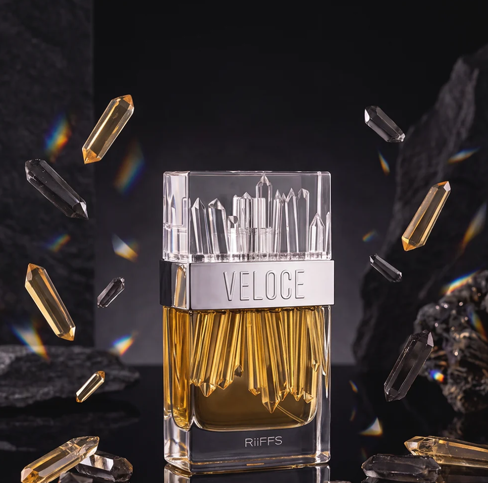 Riiffs Veloce amber-filled bottle with clear crystal-style cap and silver name band, surrounded by floating gold and dark crystal shapes against a black rocky background.
