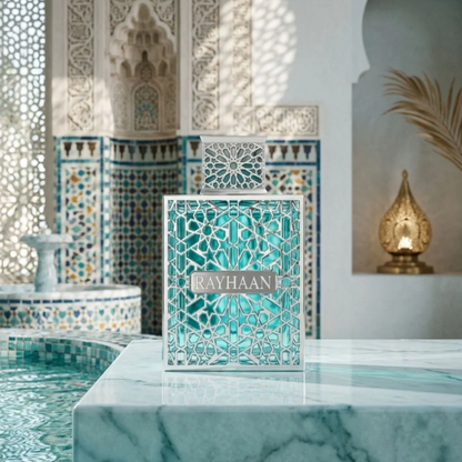 Rayhaan Aquatica turquoise bottle with silver geometric detailing and matching cap on a pale marble ledge beside a tiled pool, patterned walls and a gold-colored lamp.