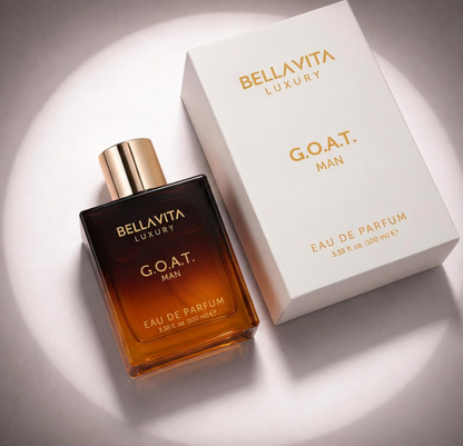 Angled overhead view of Bellavita G.O.A.T. Man amber perfume bottle with a gold cap beside its white box under a circular spotlight.