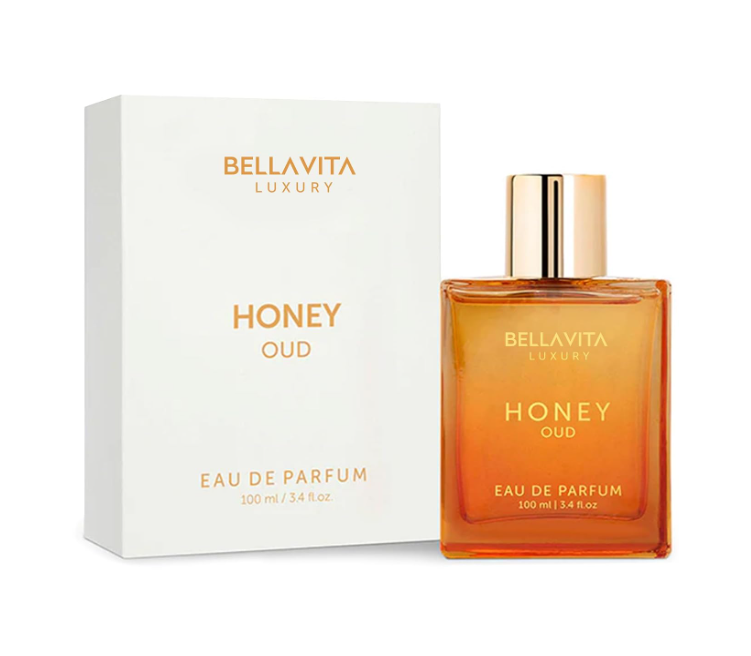 Bellavita Honey Oud clear rectangular bottle filled with amber-colored perfume, topped with a gold cap, beside its white and gold box on white.