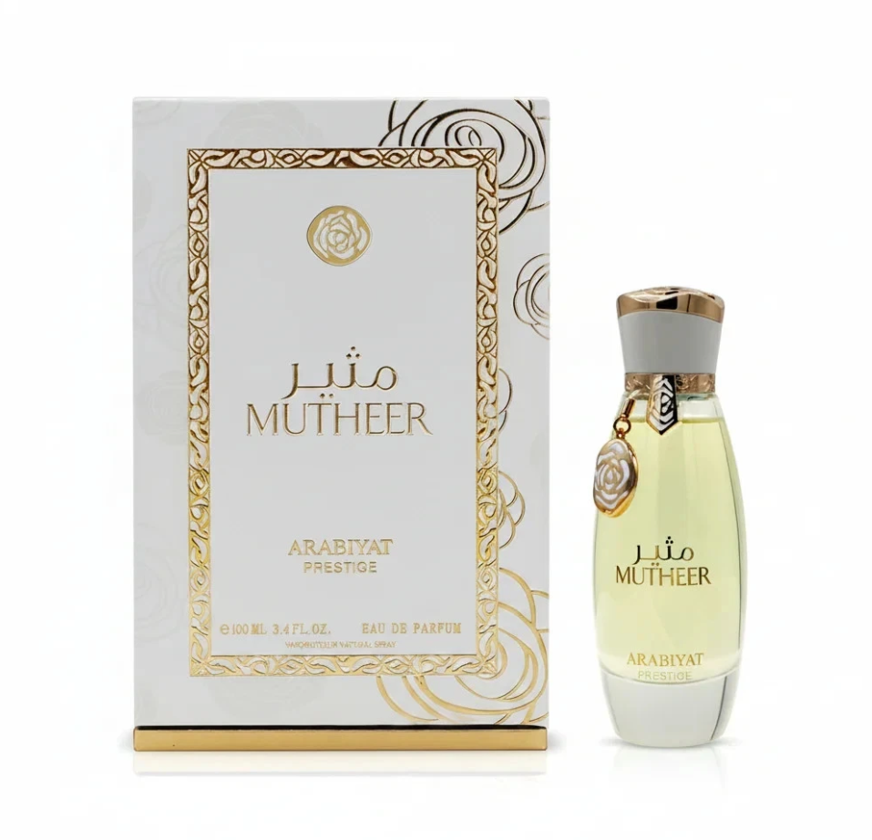 Arabiyat Prestige Mutheer pale yellow perfume in a tapered clear bottle with white-and-gold cap and hanging round charm, beside its white-and-gold patterned box on white.