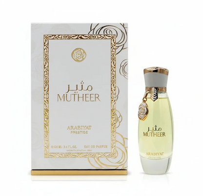 Arabiyat Prestige Mutheer pale yellow perfume in a tapered clear bottle with white-and-gold cap and hanging round charm, beside its white-and-gold patterned box on white.