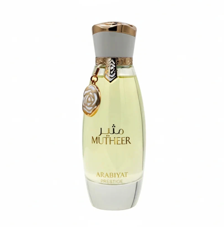 Arabiyat Prestige Mutheer tapered bottle with pale yellow liquid, white base and cap, gold trim and dangling circular floral charm, isolated on white.