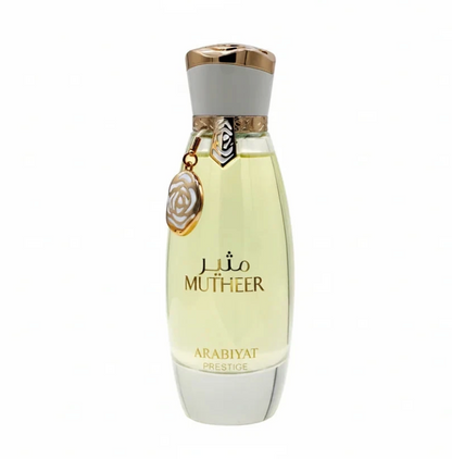 Arabiyat Prestige Mutheer tapered bottle with pale yellow liquid, white base and cap, gold trim and dangling circular floral charm, isolated on white.
