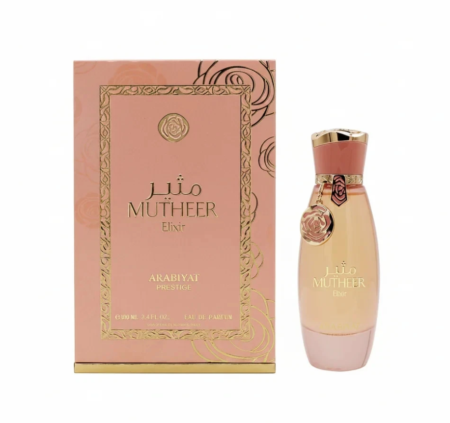 Arabiyat Prestige Mutheer Elixir peach-toned bottle with pink base, coral-and-gold cap and hanging floral charm, beside its pink-and-gold patterned box on white.