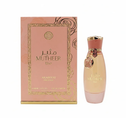 Arabiyat Prestige Mutheer Elixir peach-toned bottle with pink base, coral-and-gold cap and hanging floral charm, beside its pink-and-gold patterned box on white.