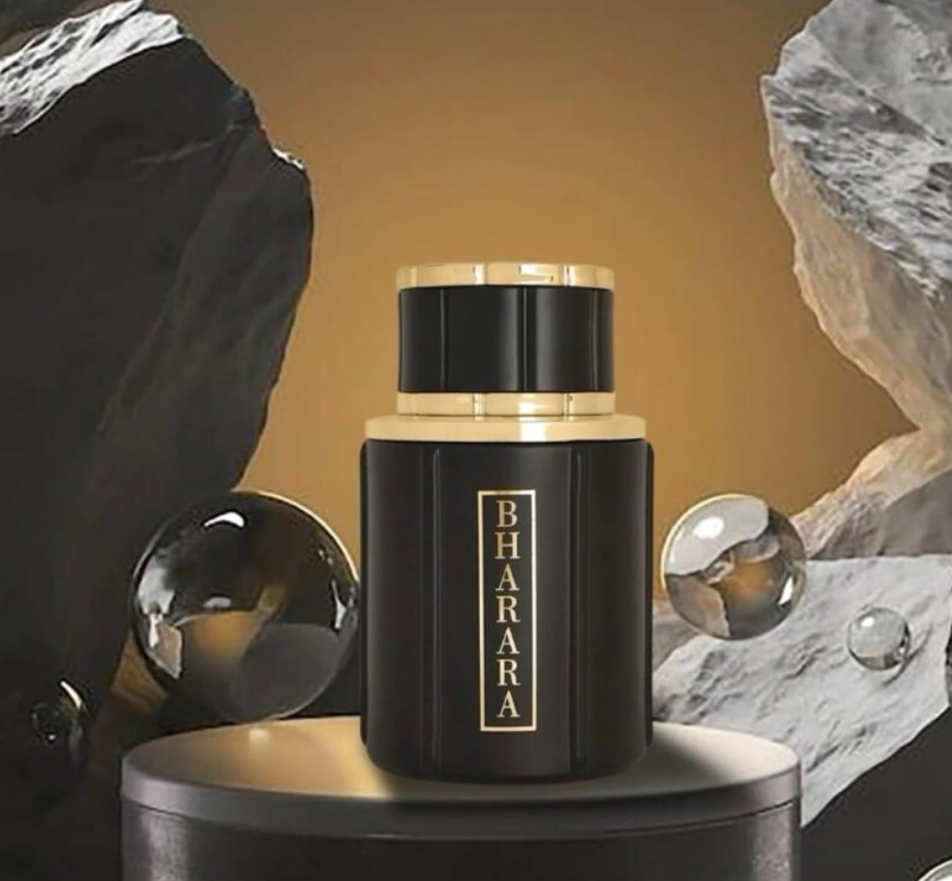 Bharara Noir Pour Homme black-and-gold bottle with a broad cap on a round dark pedestal, framed by gray rocks and reflective spheres against a warm gold background.