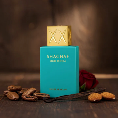 Swiss Arabian Shaghaf Oud Tonka turquoise bottle with gold cap on a wooden surface, beside almonds, dark seeds and dark pods and a red rose on a brown background.