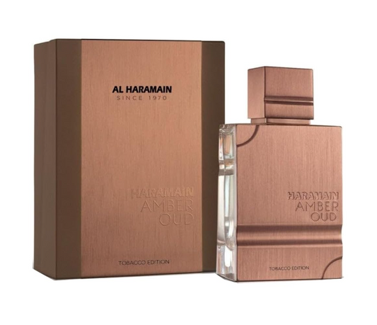Al Haramain Amber Oud Tobacco Edition copper-colored rectangular bottle with a square cap beside its matching copper and brown box on white.